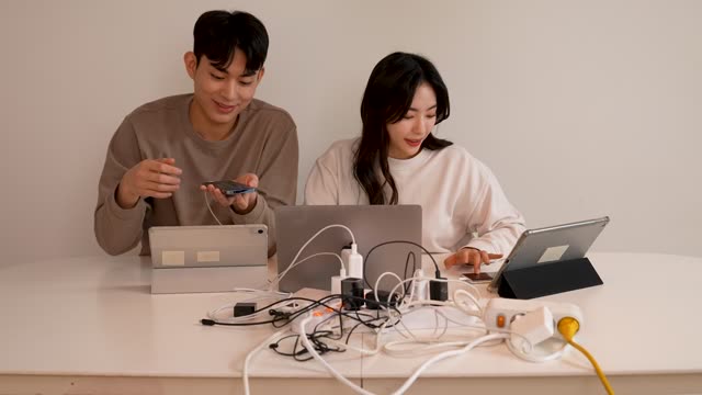 집 거실 여러 개의 콘센트를 꽂고 노트북과 태블릿피씨 스마트폰 사용하며 에너지 낭비하는 젊은커플 부부 모습