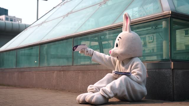 Devastated rabbit mascot performer sitting on ground while handing out ...